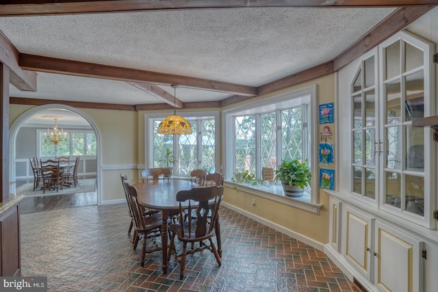 dining space featuring a wealth of natural light, a chandelier, beamed ceiling, and a textured ceiling