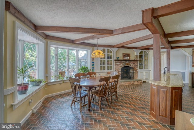 dining room with a textured ceiling, beamed ceiling, and a brick fireplace