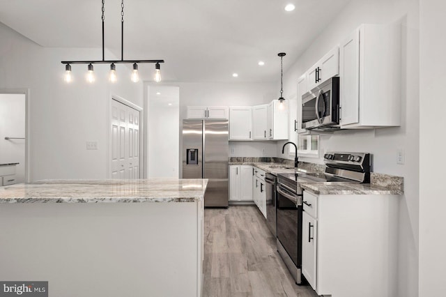 kitchen with decorative light fixtures, light stone counters, light wood-style flooring, appliances with stainless steel finishes, and white cabinets