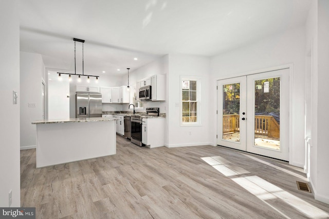 kitchen with white cabinets, a kitchen island, appliances with stainless steel finishes, light hardwood / wood-style flooring, and pendant lighting