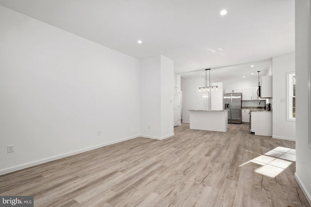 unfurnished living room with recessed lighting, light wood-type flooring, baseboards, and a sink