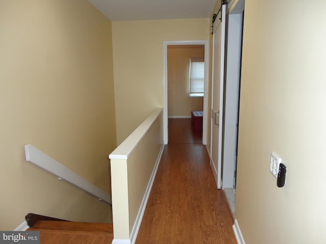 corridor with wood finished floors, baseboards, an upstairs landing, and a barn door