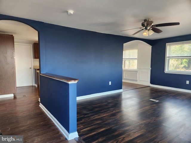 unfurnished room with ceiling fan, baseboards, arched walkways, and dark wood-style floors