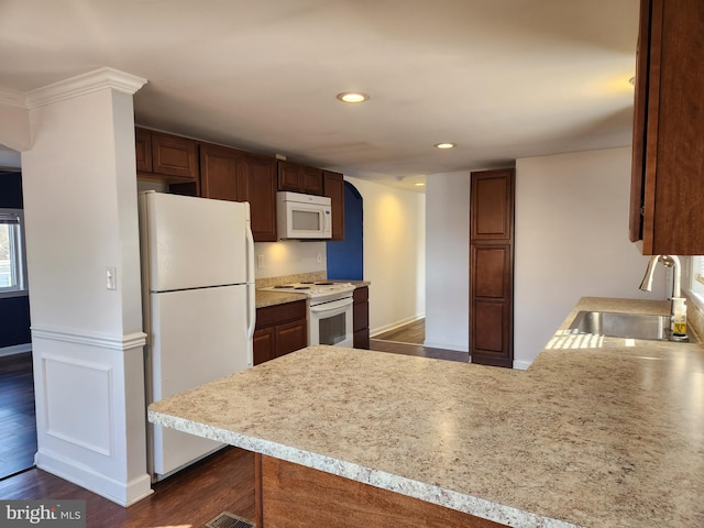 kitchen featuring white appliances, dark wood finished floors, a peninsula, a sink, and light countertops