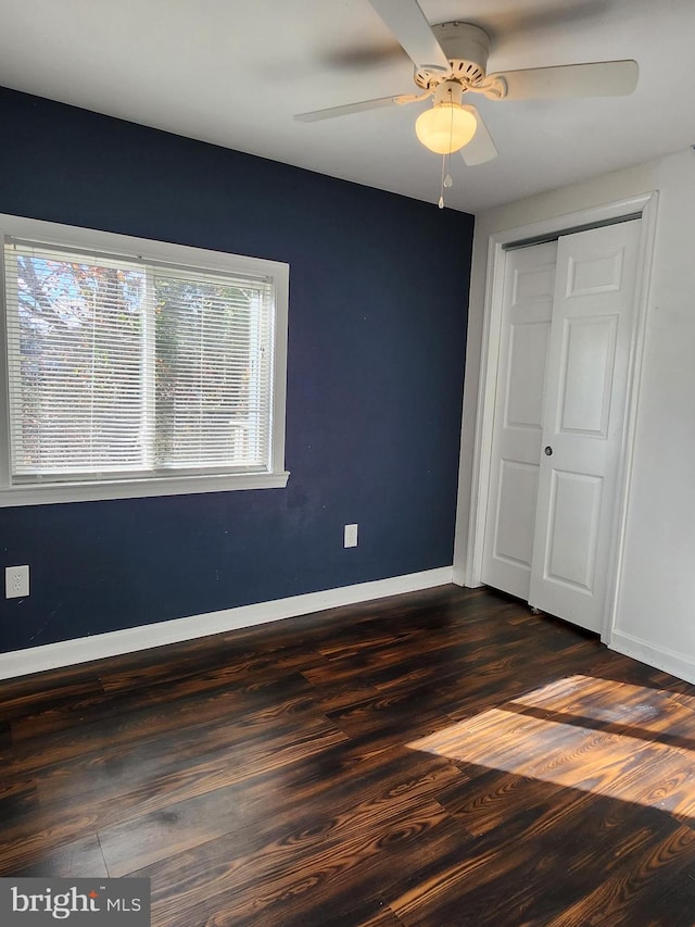 unfurnished bedroom with ceiling fan, a closet, baseboards, and dark wood finished floors