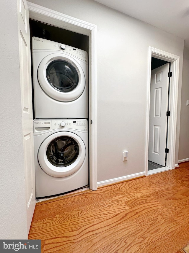 washroom with stacked washer and dryer and light hardwood / wood-style flooring