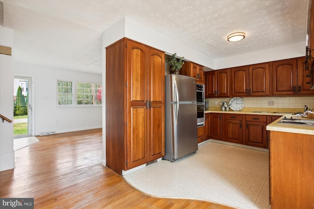 kitchen featuring light hardwood / wood-style floors, backsplash, stainless steel fridge, and a textured ceiling