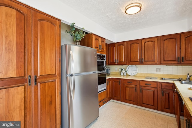 kitchen featuring tasteful backsplash, stainless steel fridge, dishwasher, sink, and a textured ceiling