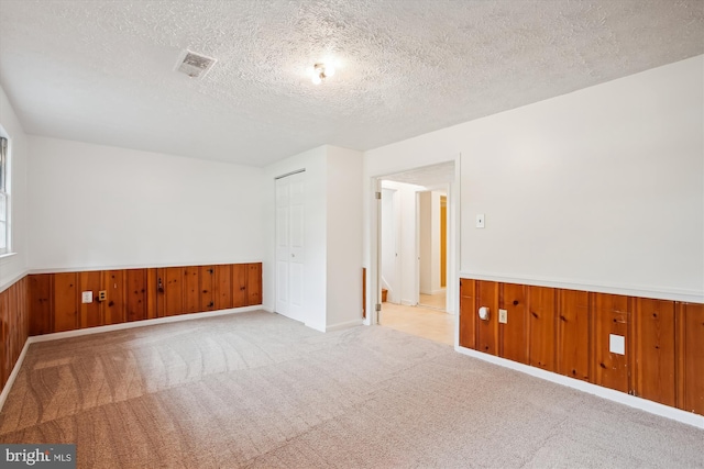 carpeted empty room featuring wood walls and a textured ceiling