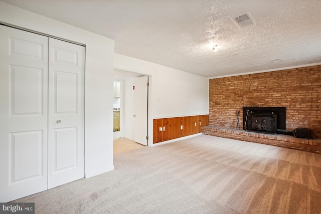 unfurnished living room featuring light carpet, a textured ceiling, wooden walls, and a brick fireplace