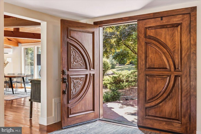 entryway featuring hardwood / wood-style floors, a wall unit AC, and beam ceiling