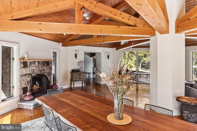 dining space with hardwood / wood-style flooring, vaulted ceiling with beams, wooden ceiling, and a stone fireplace