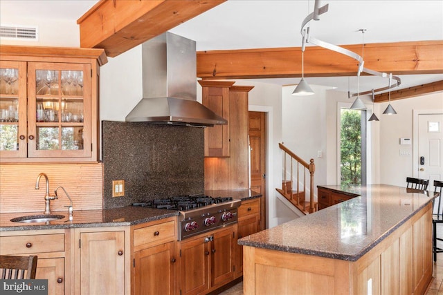 kitchen with wall chimney exhaust hood, pendant lighting, a kitchen island with sink, sink, and decorative backsplash