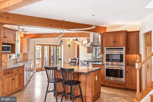 kitchen with a kitchen bar, stainless steel appliances, sink, hanging light fixtures, and wall chimney range hood