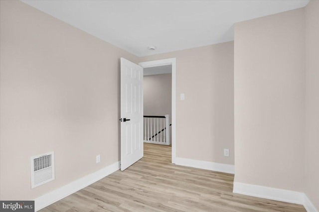 empty room with visible vents, light wood-type flooring, and baseboards