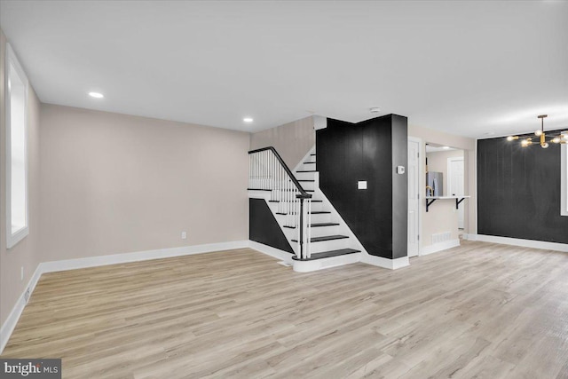 empty room featuring a notable chandelier, light wood-style flooring, stairs, and baseboards