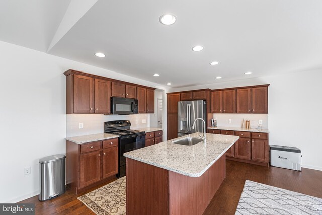 kitchen with black appliances, dark hardwood / wood-style flooring, an island with sink, sink, and light stone countertops