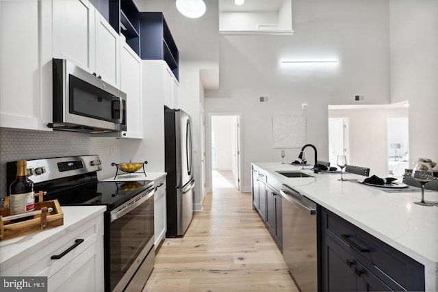 kitchen with a high ceiling, white cabinets, stainless steel appliances, and sink