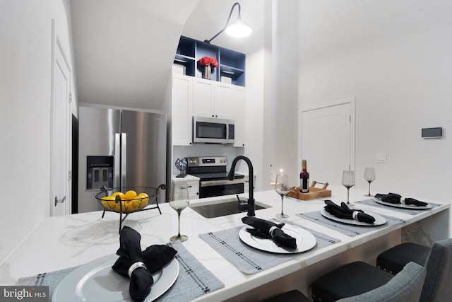 kitchen with a kitchen breakfast bar, white cabinetry, stainless steel appliances, and sink