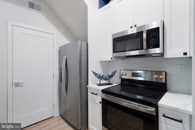 kitchen with light hardwood / wood-style flooring, backsplash, appliances with stainless steel finishes, light stone counters, and white cabinets