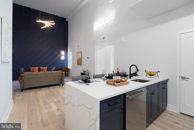 kitchen with light hardwood / wood-style flooring, kitchen peninsula, light stone counters, sink, and stainless steel dishwasher