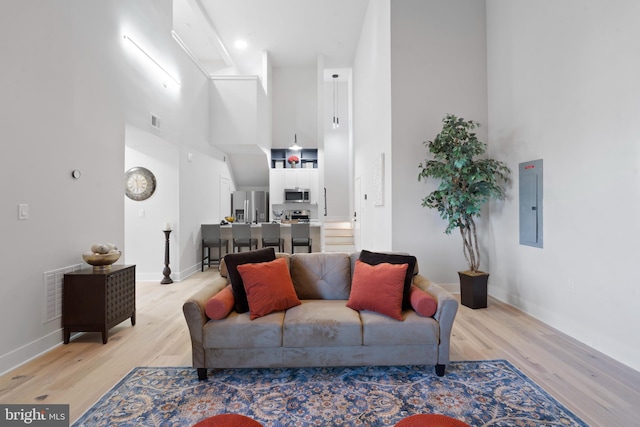 living room featuring a towering ceiling, electric panel, and light hardwood / wood-style flooring