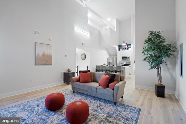 living room featuring beamed ceiling, light hardwood / wood-style flooring, and a high ceiling