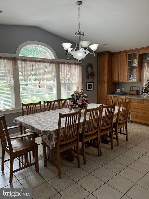 dining space with a notable chandelier, lofted ceiling, and light tile patterned floors