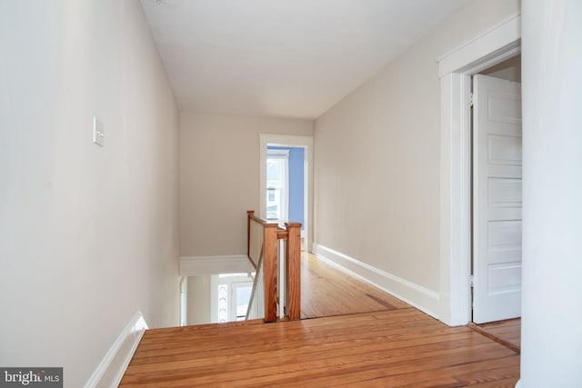 corridor featuring wood finished floors, an upstairs landing, and baseboards