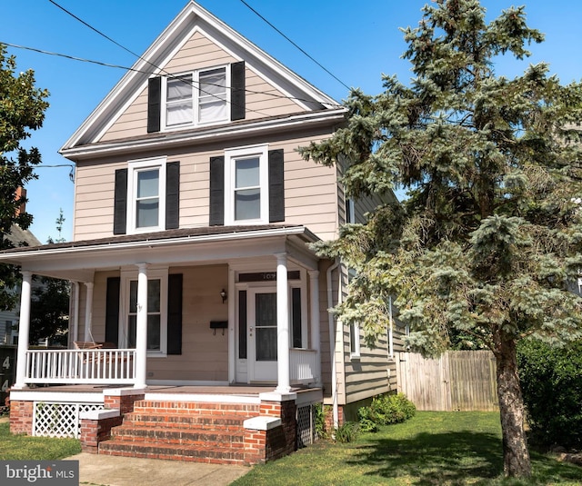 view of front of home featuring covered porch, a front yard, and fence