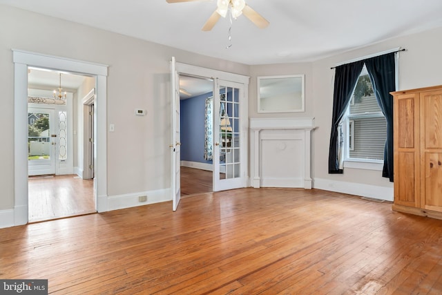 interior space featuring light wood-style flooring, ceiling fan with notable chandelier, and baseboards