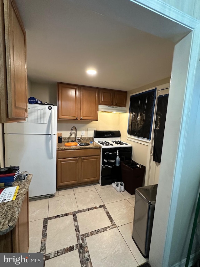 kitchen with white appliances, dark stone countertops, and sink