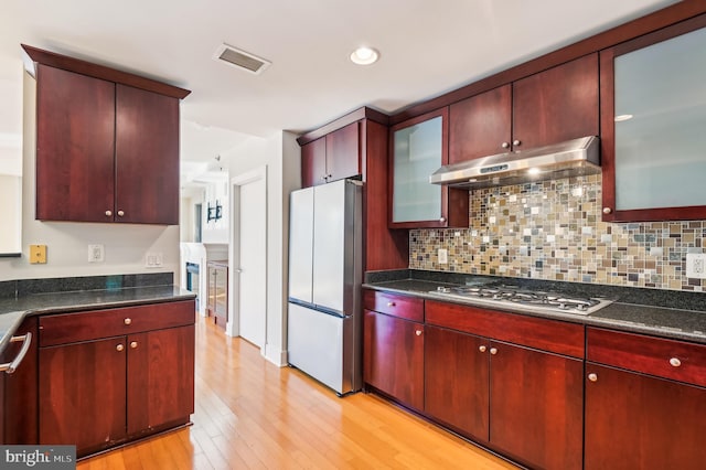 kitchen with backsplash, dark stone countertops, stainless steel appliances, and light hardwood / wood-style floors