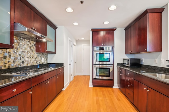 kitchen with stainless steel appliances, backsplash, dark stone countertops, extractor fan, and light wood-type flooring