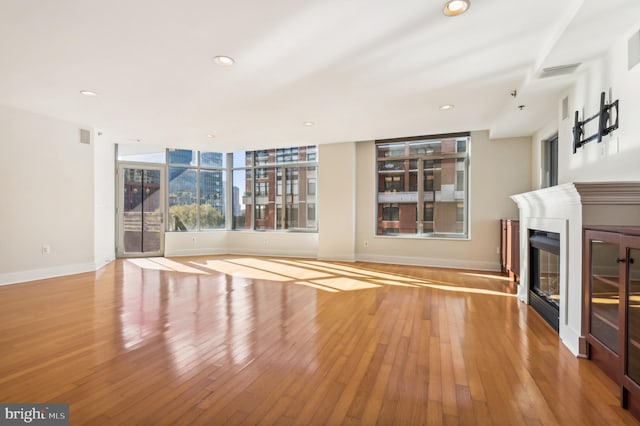 unfurnished living room featuring recessed lighting, light wood-style flooring, baseboards, and a glass covered fireplace