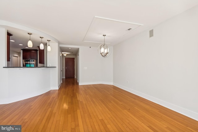 unfurnished living room featuring light wood finished floors, an inviting chandelier, visible vents, and baseboards