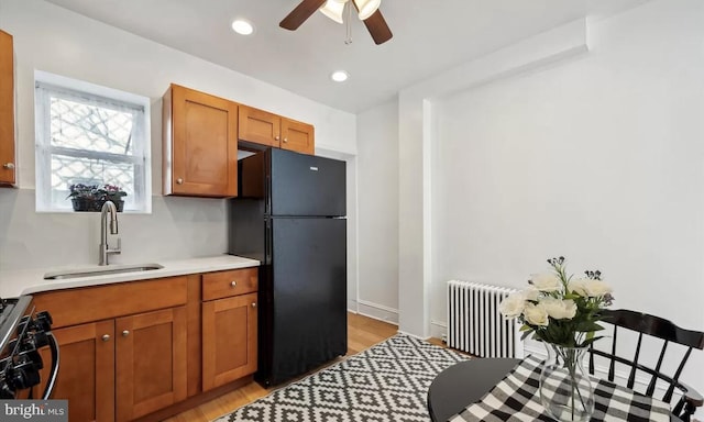 kitchen with range with gas stovetop, radiator heating unit, freestanding refrigerator, a sink, and brown cabinets