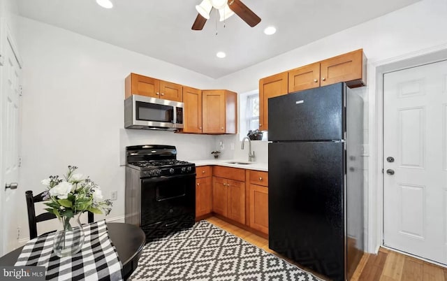 kitchen featuring a sink, black appliances, light countertops, light wood-style floors, and brown cabinets