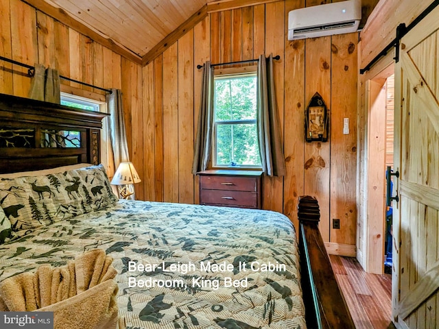 bedroom featuring a wall mounted AC, wood-type flooring, vaulted ceiling, a barn door, and wood walls