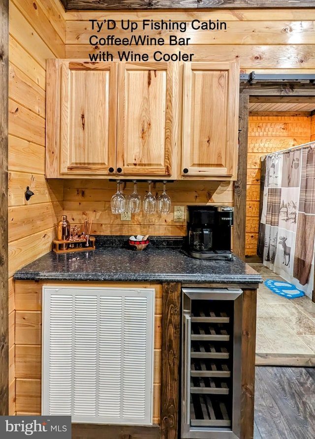 bar featuring wood walls, light brown cabinetry, dark stone countertops, and beverage cooler