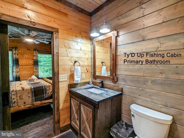 bathroom with toilet, ceiling fan, vanity, and wooden walls