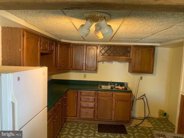 kitchen featuring a sink, a paneled ceiling, brown cabinetry, and freestanding refrigerator