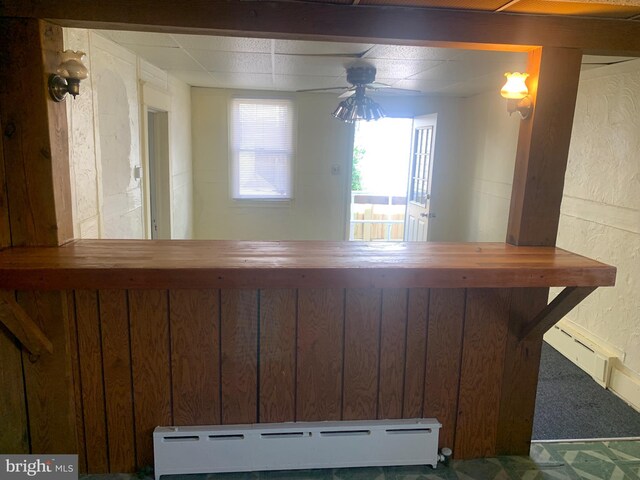 bar with ceiling fan, a baseboard radiator, and wooden walls