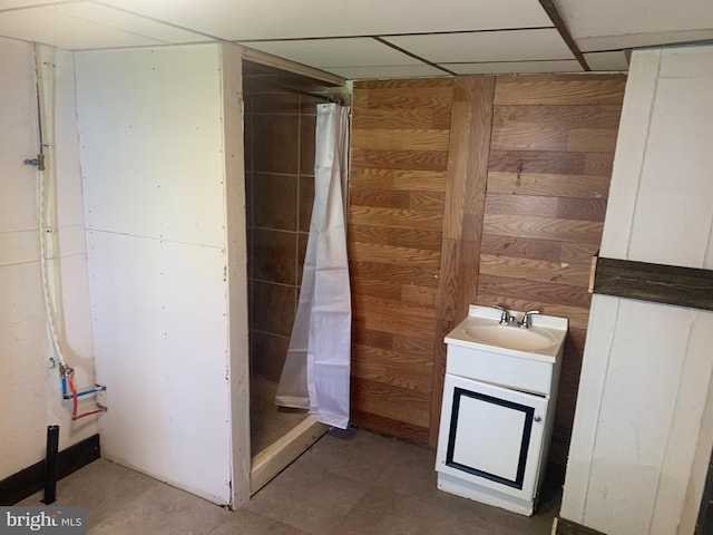 bathroom with vanity, a shower stall, wooden walls, and a drop ceiling