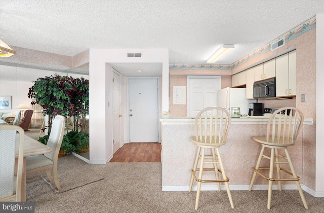 kitchen with white cabinetry, white refrigerator, a textured ceiling, wood-type flooring, and a kitchen bar