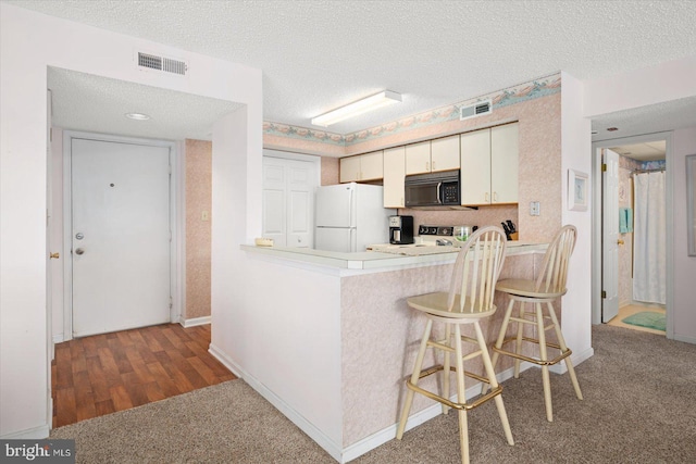 kitchen with a textured ceiling, kitchen peninsula, a kitchen bar, white fridge, and light hardwood / wood-style flooring