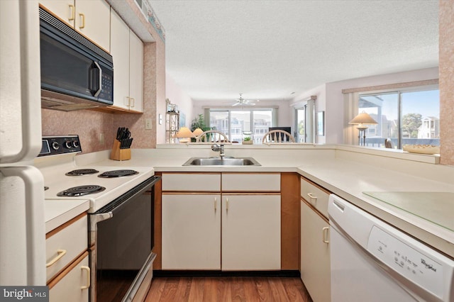 kitchen with white cabinets, kitchen peninsula, sink, white appliances, and light hardwood / wood-style floors