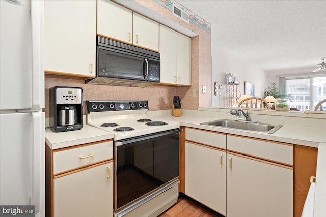 kitchen with a textured ceiling, white appliances, sink, and light hardwood / wood-style flooring