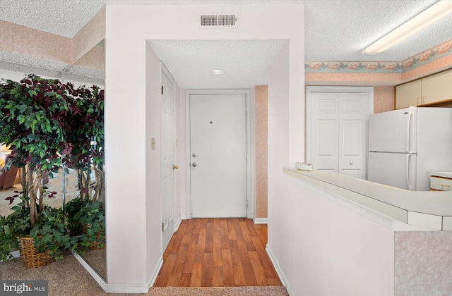 hallway with light wood-type flooring and a textured ceiling