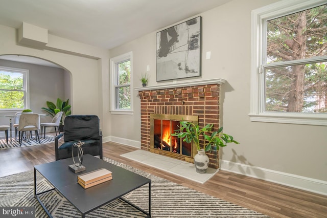 living room with a brick fireplace, a wealth of natural light, and hardwood / wood-style flooring